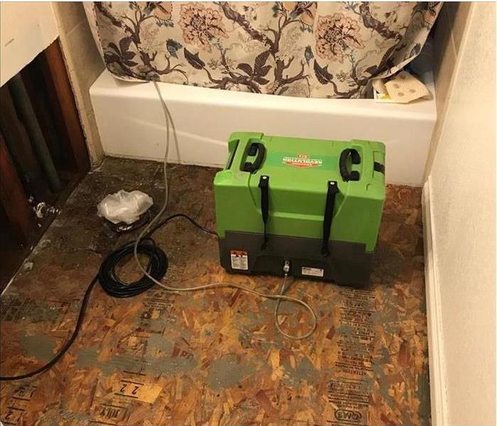 A flooded bathroom is being cleaned by restoration machines